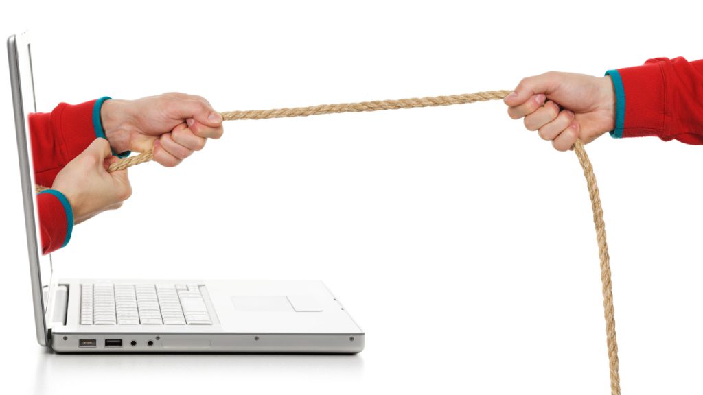 A pair of hands emerging from a laptop play tug of war with another hand.