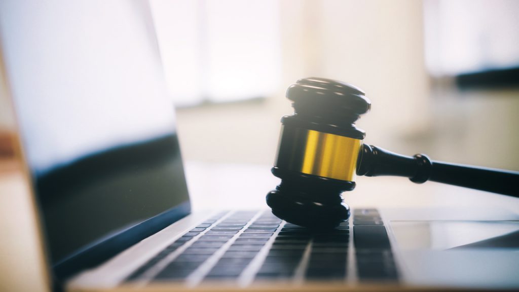 A judge's gavel resting on a laptop computer.