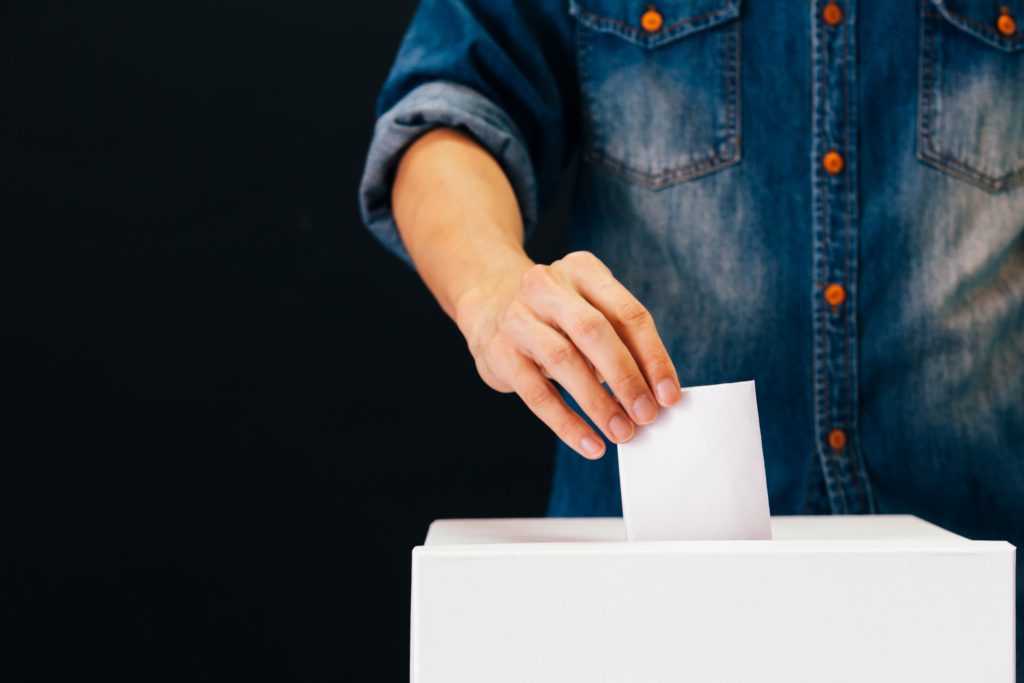 A hand placing a ballot into a ballot box.