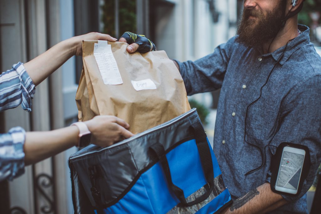 A man recieves a food delivery order in a brown paper bag.