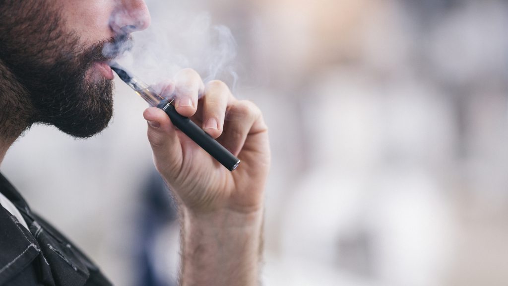 A bearded man smokes an electronic cigarette.