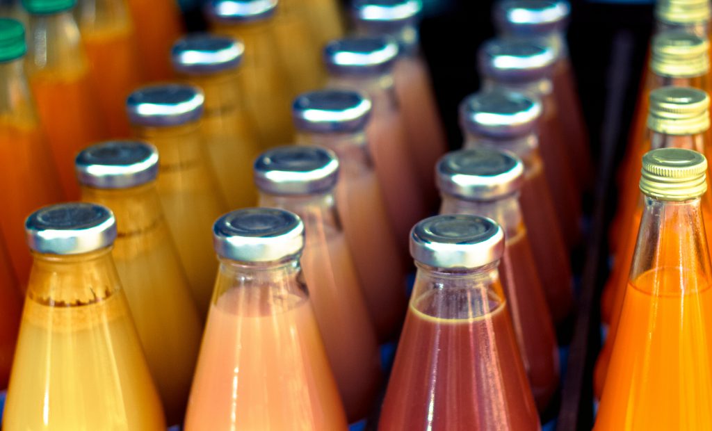 A dozen bottles of juice in various colors.